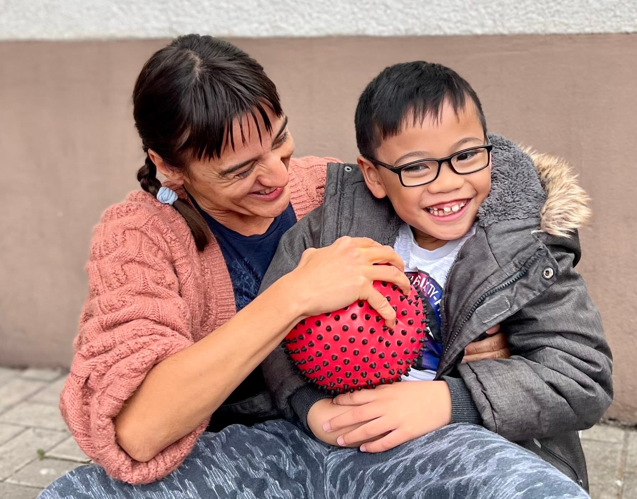 Veneta und ein Kind sitzen mit einem roten Ball zusammen.